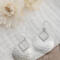 Pair of sterling silver hammered pear dangle earrings displayed on a white fabric with flowers in the background.

